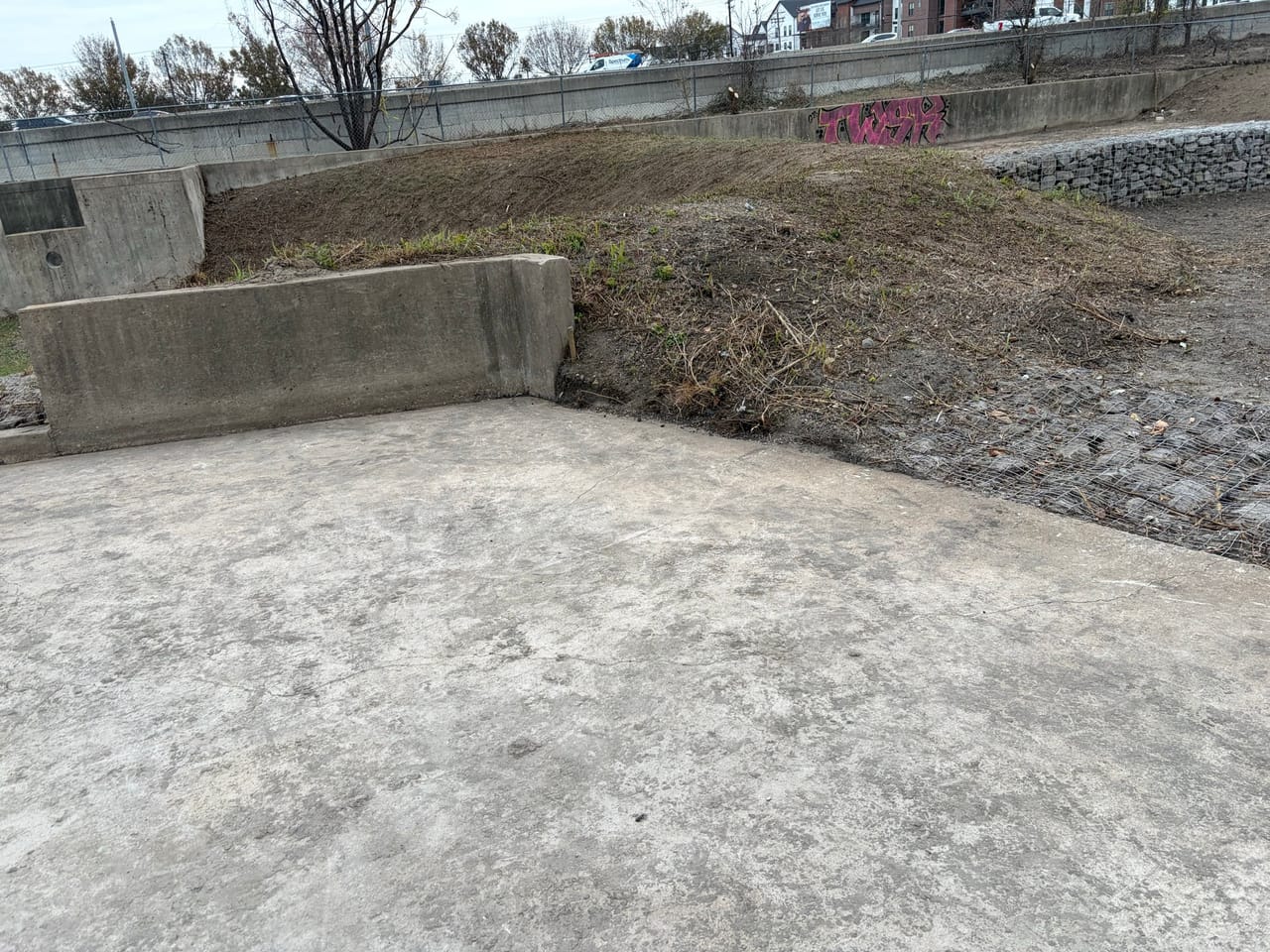 Concrete channel and graded dirt basin behind a chain link fence by Corral Bros in Central Texas