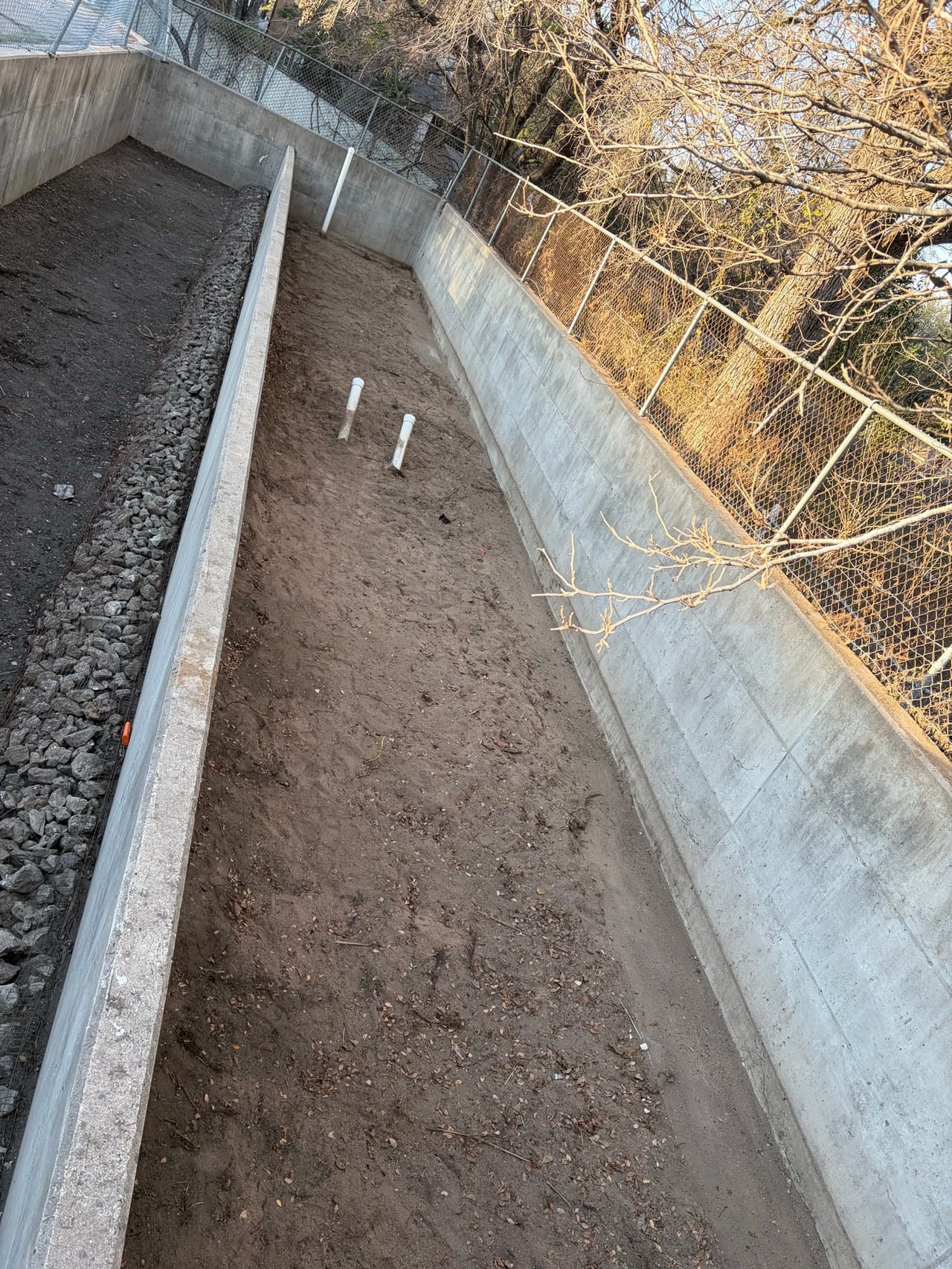 Concrete drainage channel with rock lined bottom below a chain link fence in Lakeway, TX