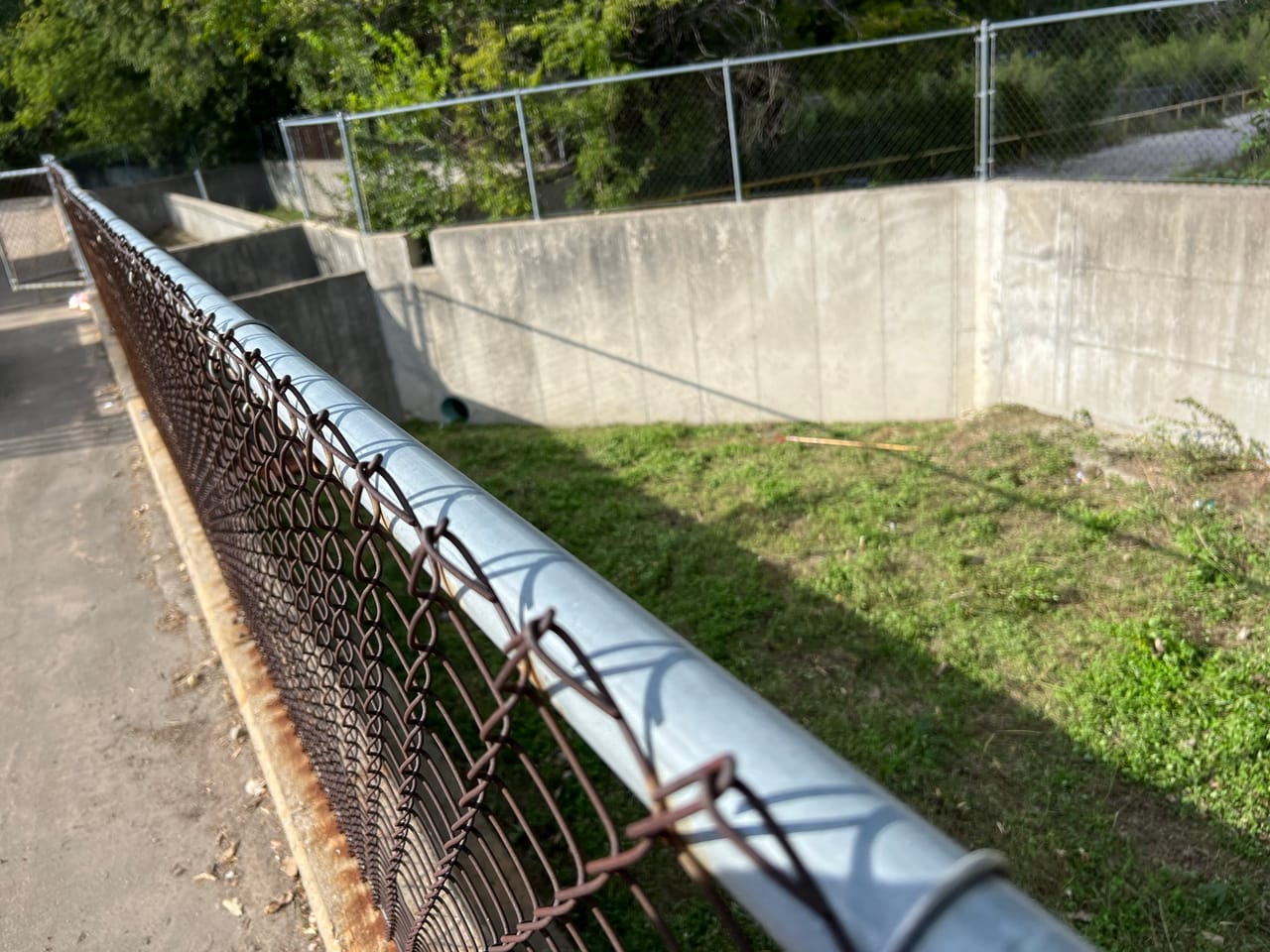 Concrete stormwater channel with chain link fence and large pipe in Central Texas