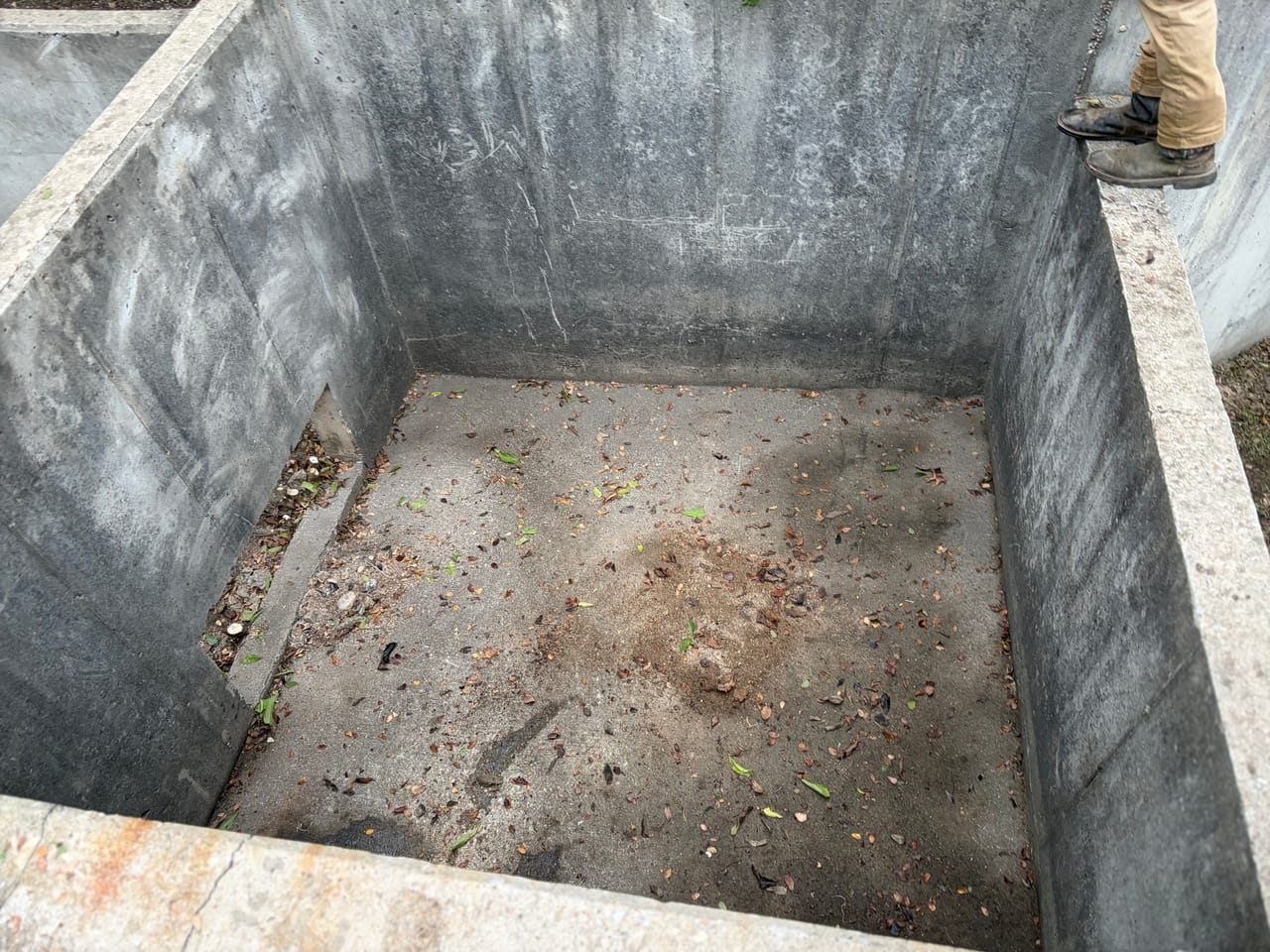 Deep concrete detention vault cleaned out with worker boots at edge in Central Texas