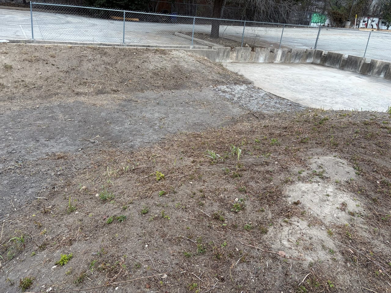 Detention basin with patchy new grass meeting a concrete channel by Corral Bros in Central Texas