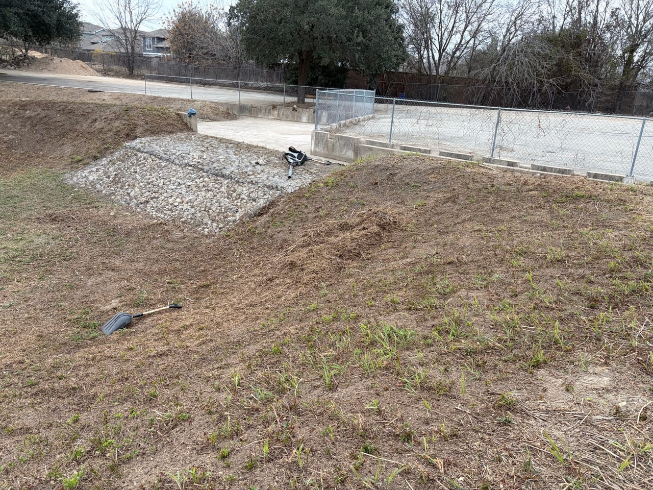 Detention basin with rock lined outfall and chain link fence behind in Marble Falls, TX