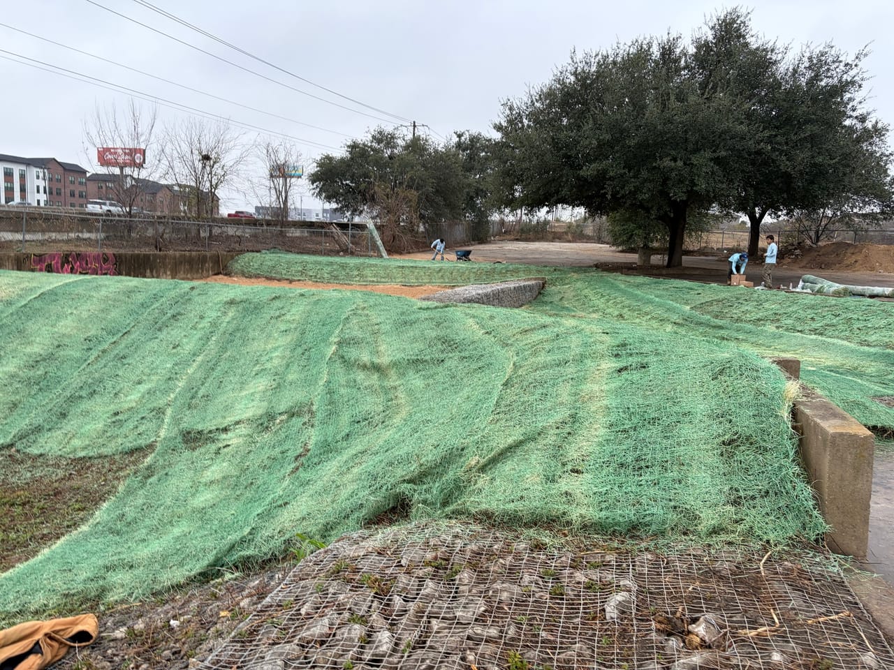 Finished erosion blanket over a wide graded slope with trees behind in Buda, TX