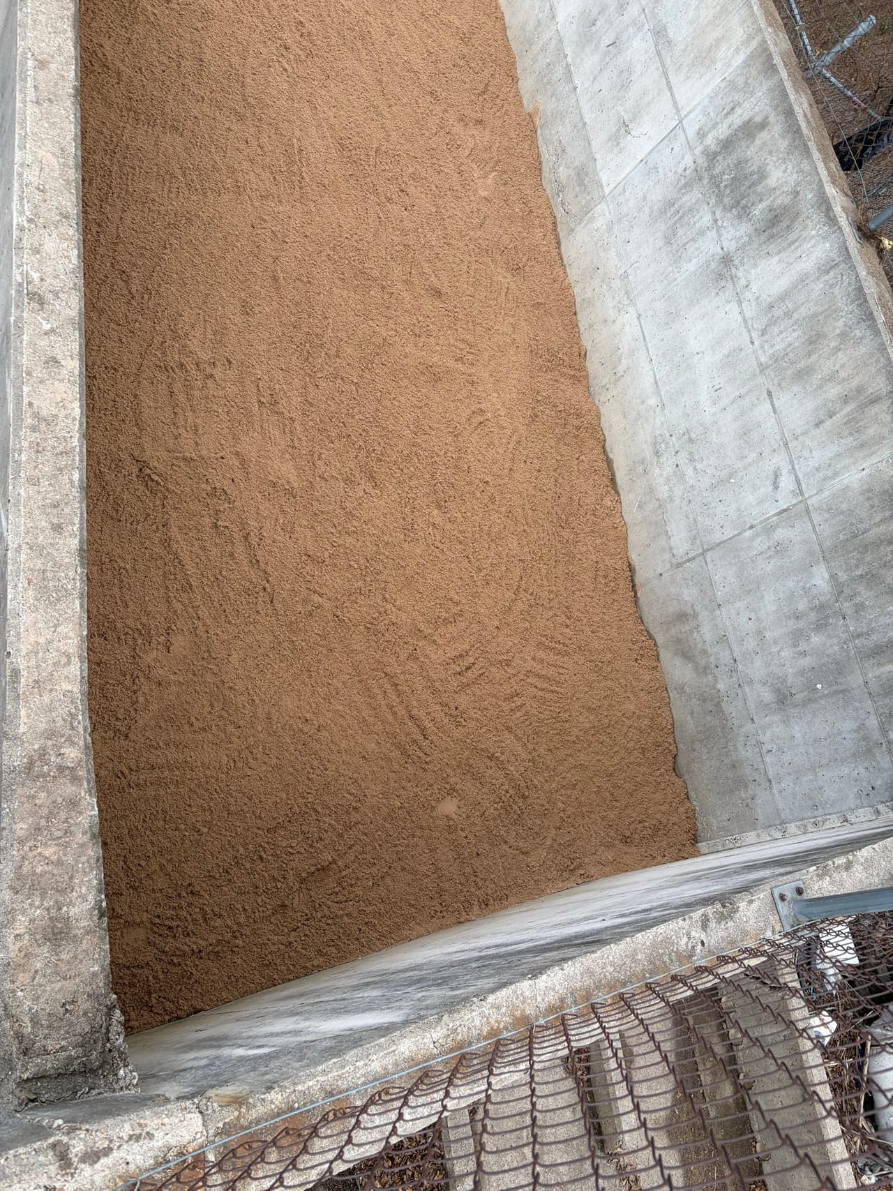 Fresh tan soil packed into a concrete channel slope by the fence in Austin, TX