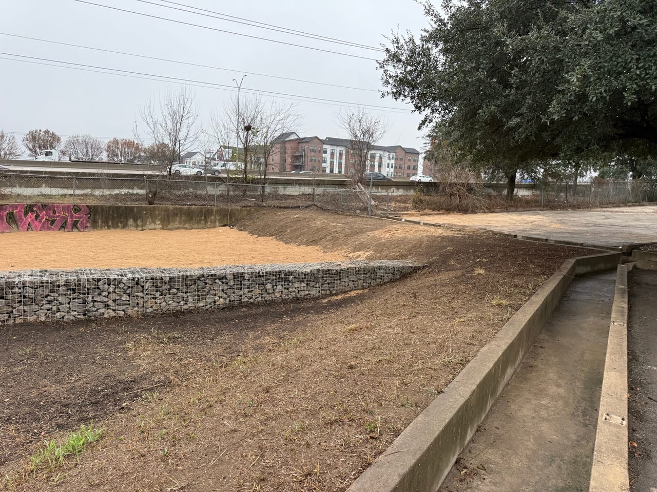 Gabion wall and concrete flume with graded slopes and trees behind in Central Texas