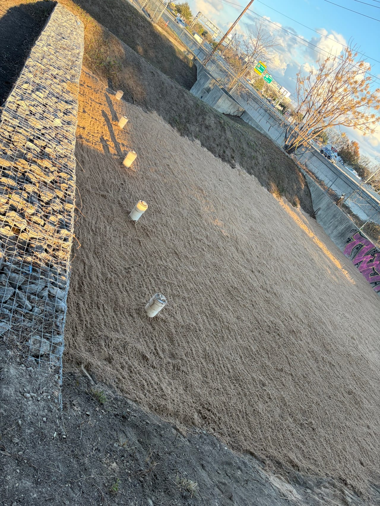 Graded dirt slope above a gabion rock basket wall, tilted framing in Georgetown, TX