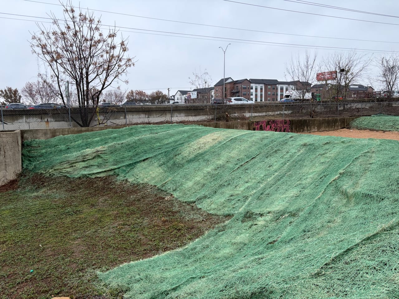Green erosion blanket covering both graded slopes of the concrete channel in Kyle, TX