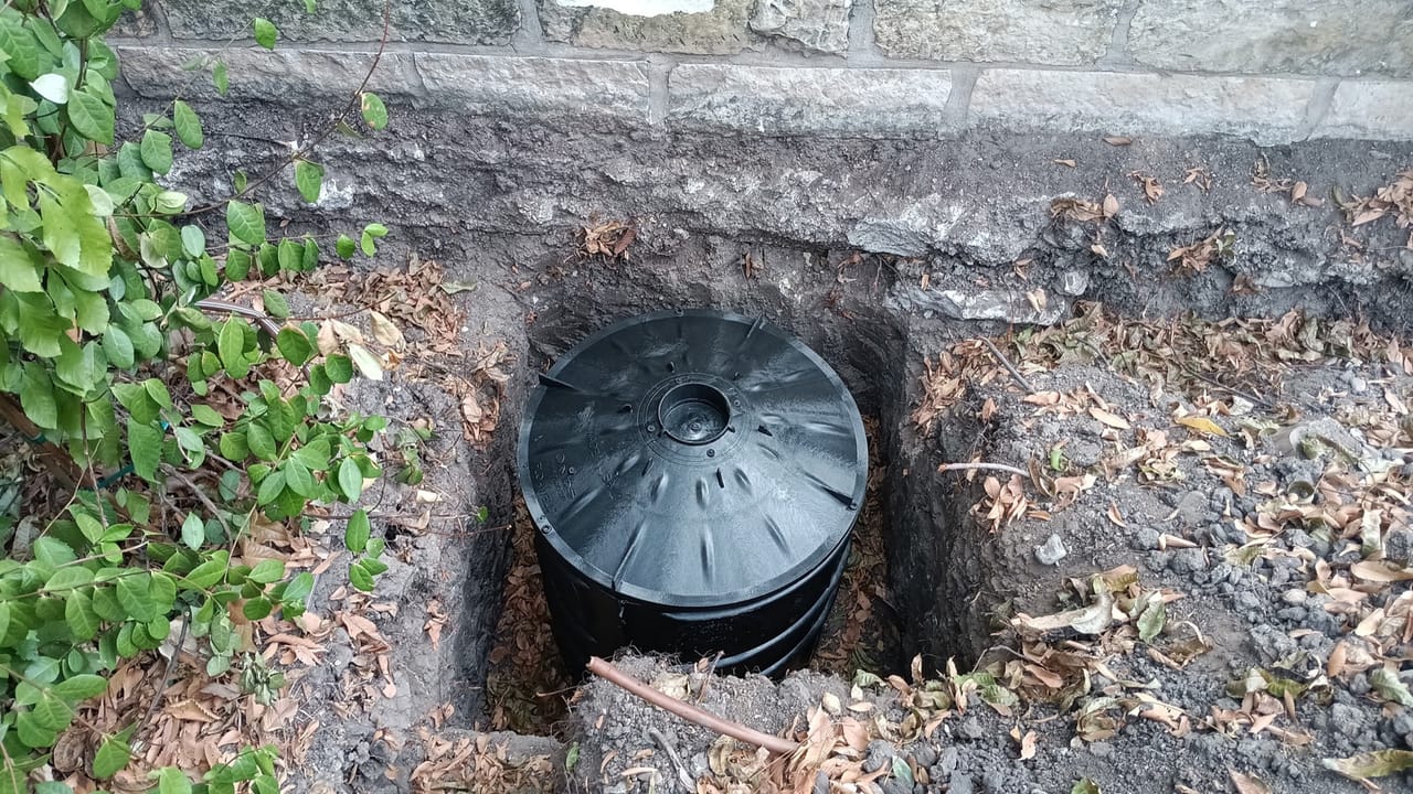 Large black detention tank set into an excavated pit against a stone wall in Buda, TX