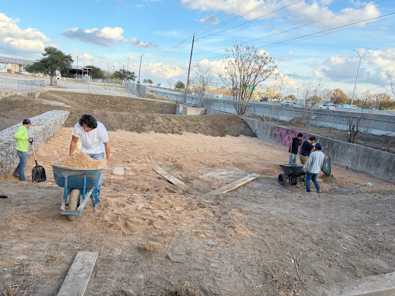 Two workers spreading soil with wheelbarrows in a concrete drainage channel in Leander, TX