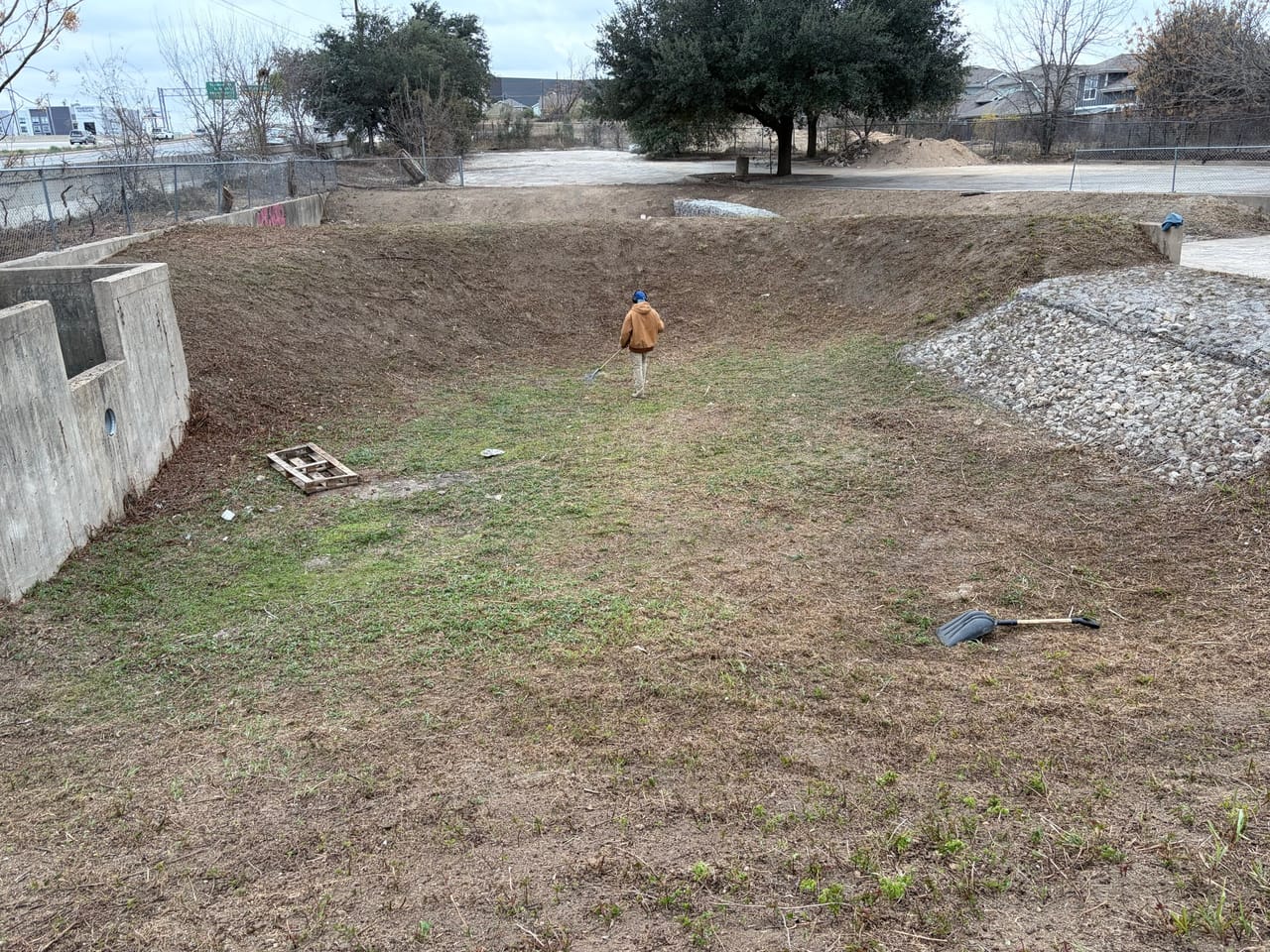 Wide detention basin with rock chutes, trees and a worker walking through in Pflugerville, TX
