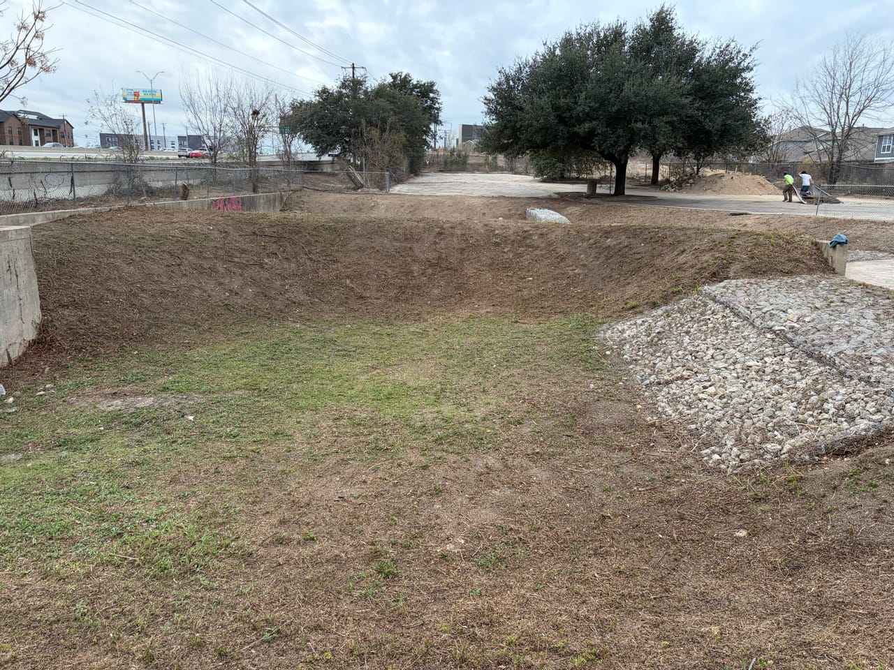 Wide seeded detention basin with rock spillways and mature trees in Central Texas