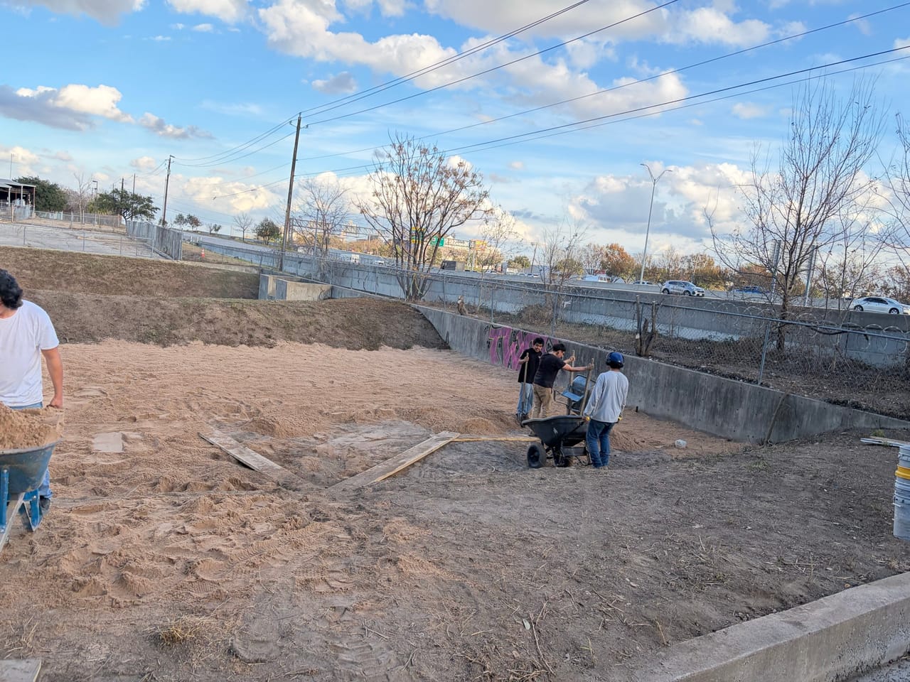 Worker pushing a wheelbarrow of soil across the bare channel bottom in Central Texas