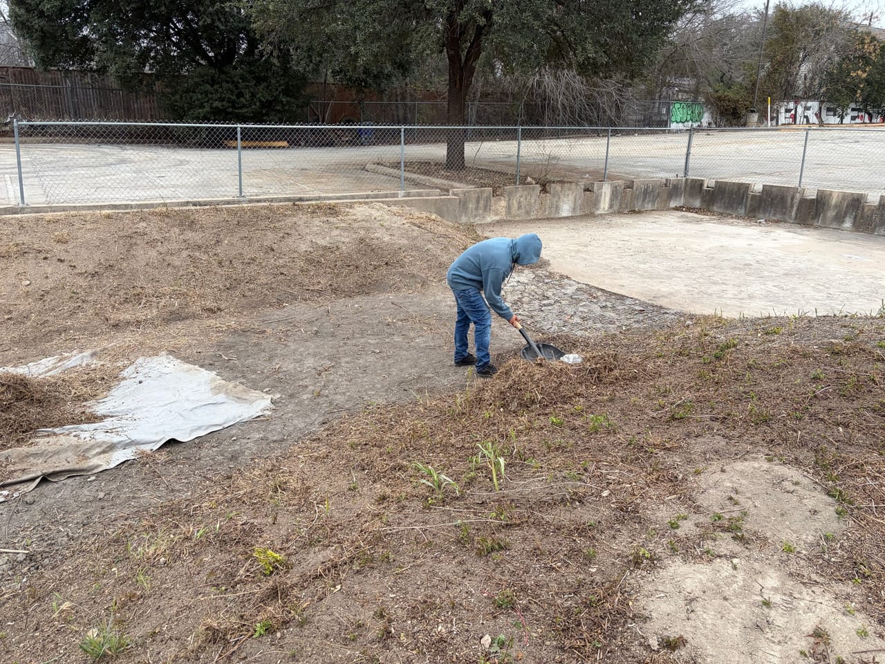 Worker raking soil and erosion blanket into a planted detention basin in New Braunfels, TX