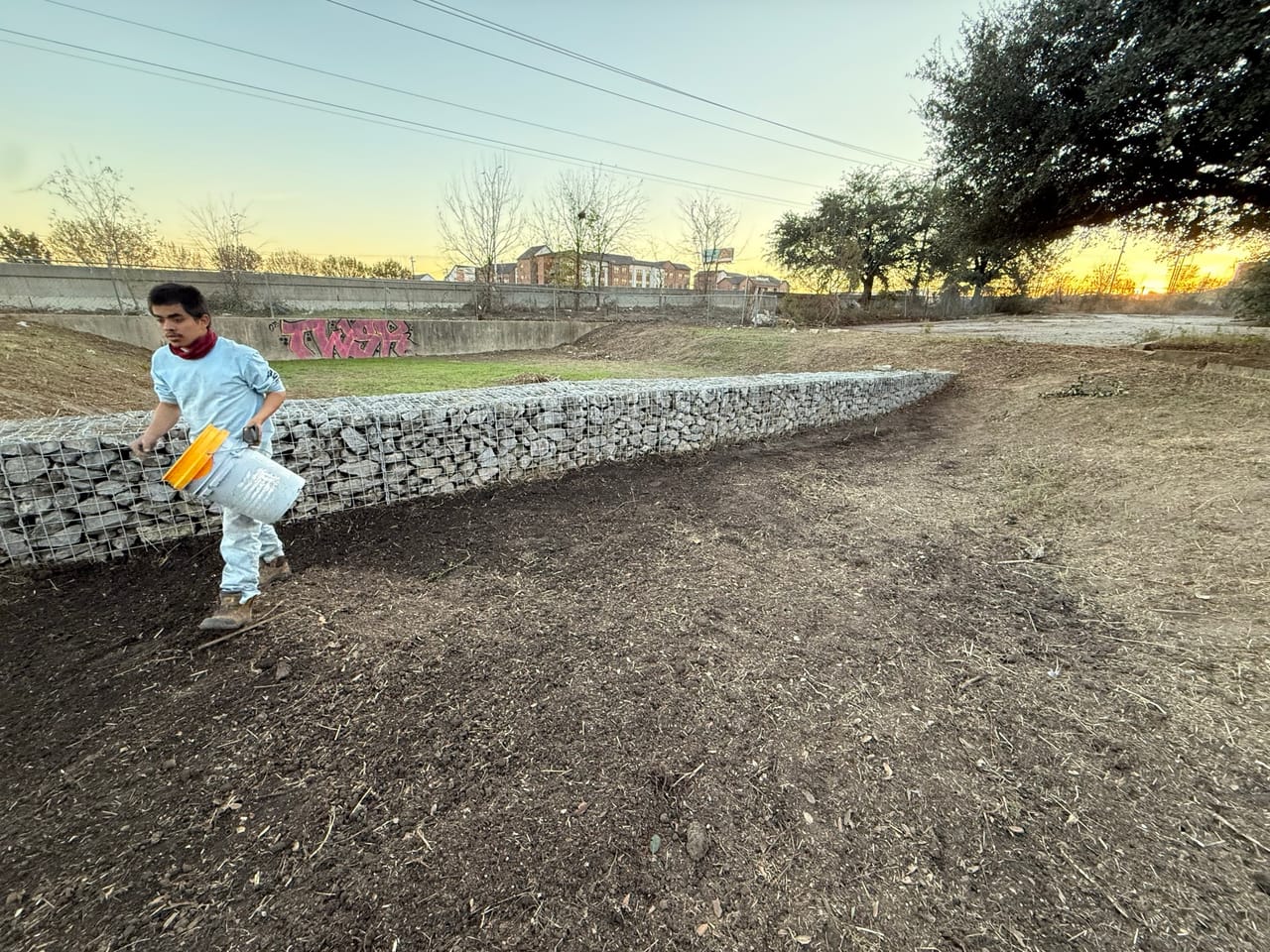 Worker walking along a freshly built rock gabion channel bank in Bastrop, TX