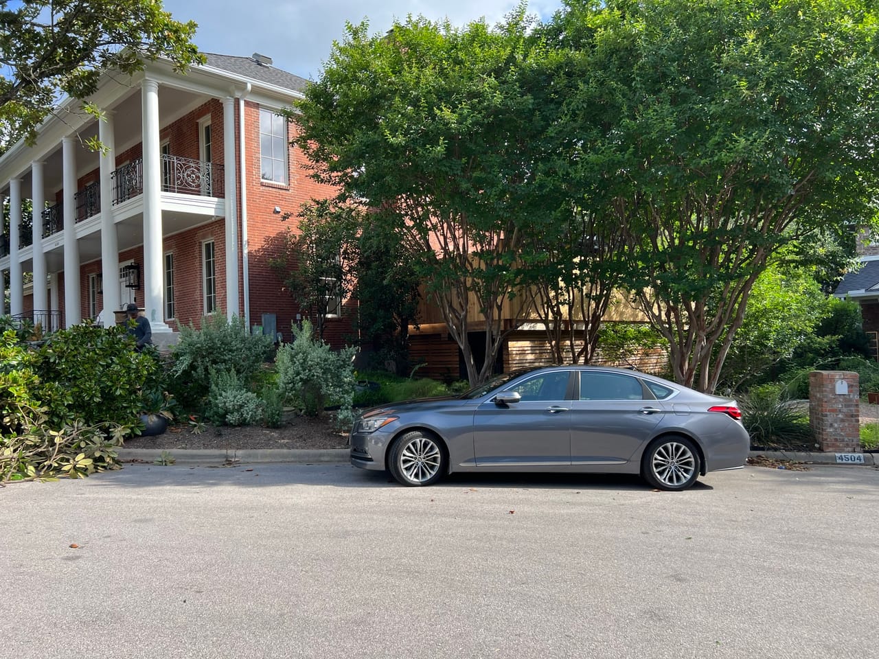 Brick colonial home front yard with trees and a parked sedan in Taylor, TX