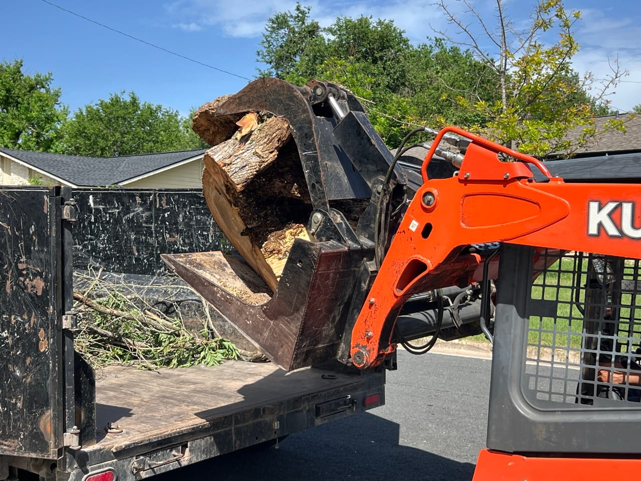 Kubota skid steer grapple loading a big log into a dump trailer in Leander, TX